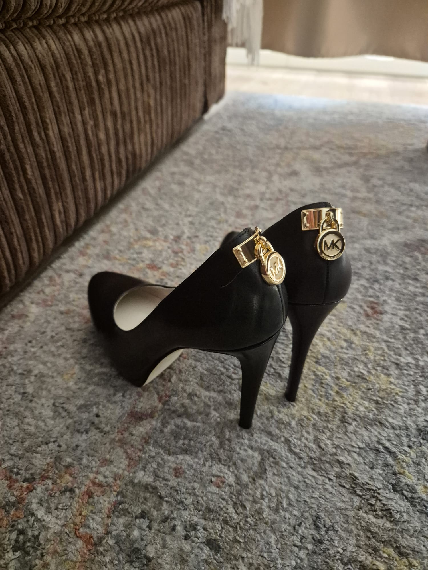 Elegante zwarte naaldhakken met gouden Michael Kors (MK) slot-details aan de achterkant